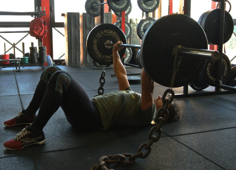 Atleta che esegue floor press con catene: l'importanza della varietà nell'allenamento.