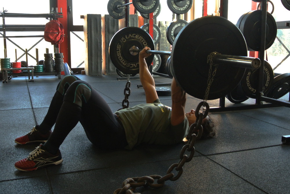 Atleta che esegue floor press con catene: l'importanza della varietà nell'allenamento.