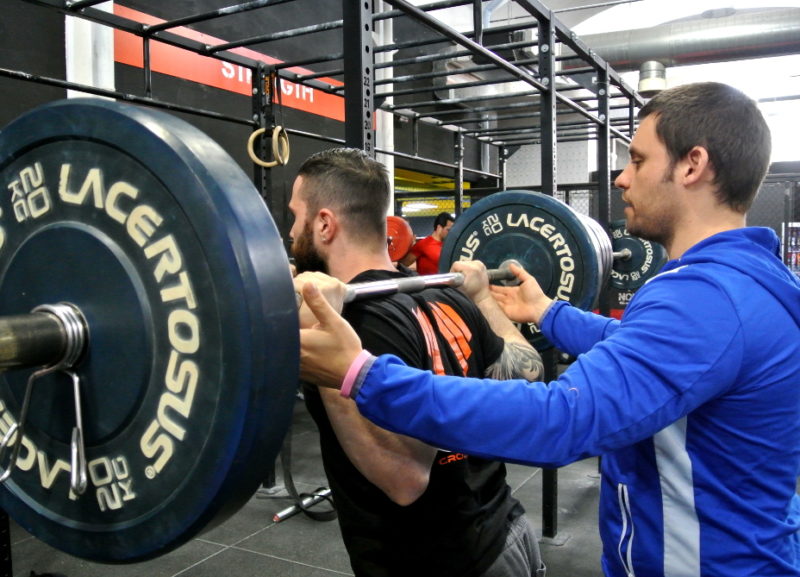 powerlifting raw: atleta che fa squat con trainer